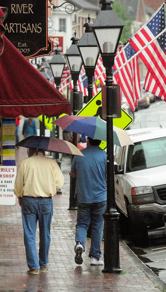 People with umbrellas walk down Water Street in Hallowell today.