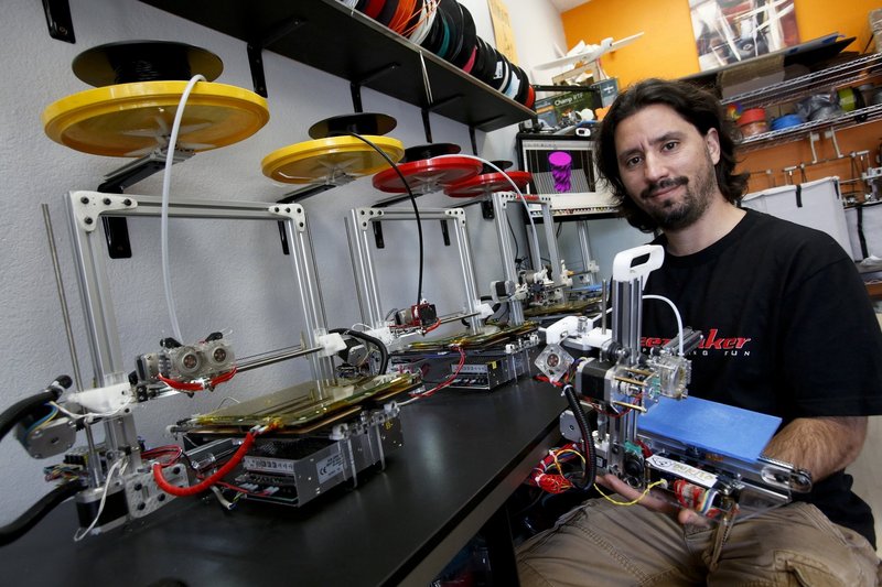 Diego Porqueras holds a Bukito 3-D printer. Bukobot 3-D printers sit on the counter.