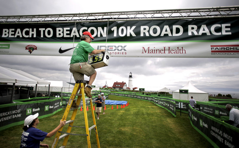 Steven Bedsole of Granite State Race Services installs the timing clock at the finish line of the TD Beach to Beacon 10K on Friday at Fort Williams Park in Cape Elizabeth. Holding the ladder is Anita Teschek.
