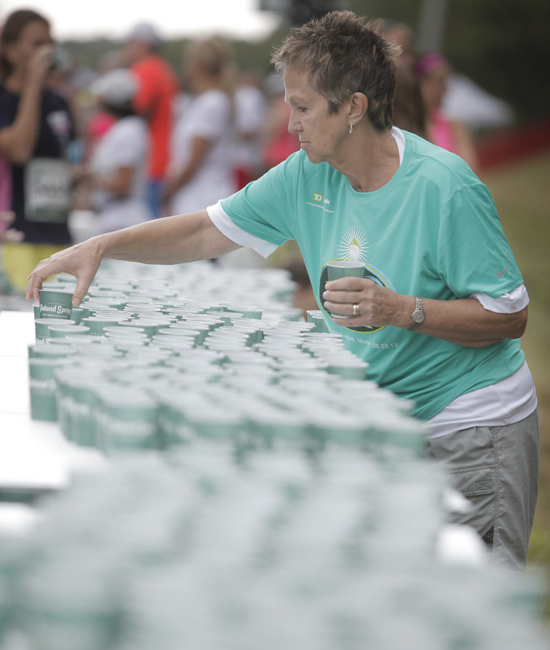 Volunteer Sue Howe of Scarborough places cups of water on a table in the staging area behind the starting line.