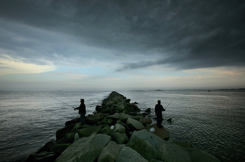 With a storm front moving in overhead, two anglers fish from the jetty at Camp Ellis. The 6,600-foot jetty, with the ocean on the left side and the mouth of the Saco River on the right, is a popular location for striper fishing. Over many decades, it also has been the primary cause of severe erosion requiring a costly fix.