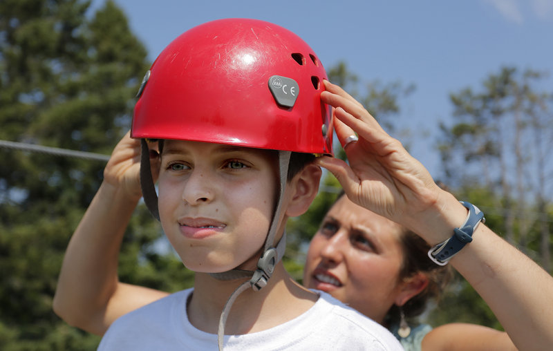 Salar Salim, 12, of Portland, originally from Iraq, gets some help from Ayla Zeimer getting his helmet on right for the zip line.