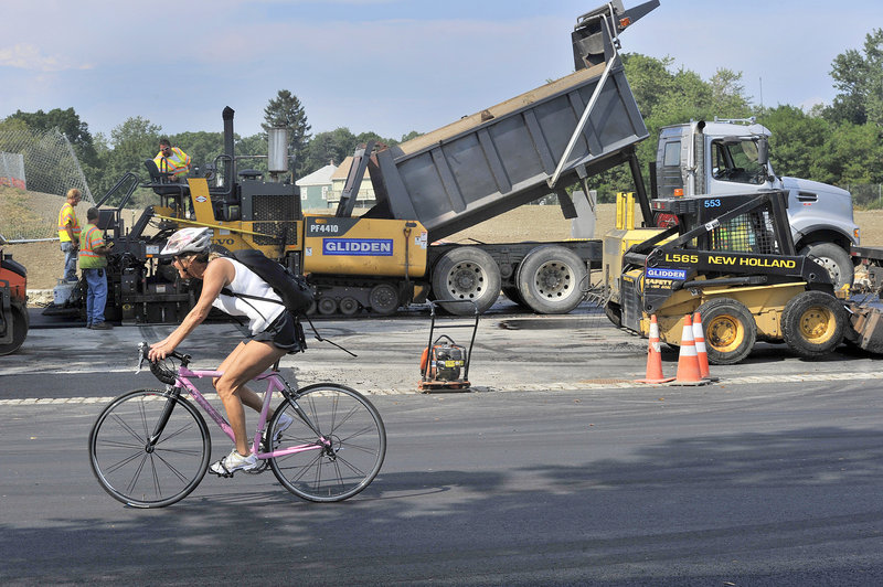 A bicyclist rides on the recently paved Baxter Boulevard as workers pave a parking area Wednesday, Aug. 28, 2013. The boulevard will reopen soon after an eight-month closure.