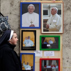 A nun walks next to pictures of newly elected Pope Francis and one of Pope Emeritus Benedict XVI near the Vatican