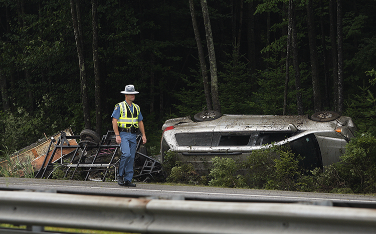 A Maine state trooper walks past a vehicle that rolled over on Interstate 295 in Freeport on Friday. One person was hospitalized.