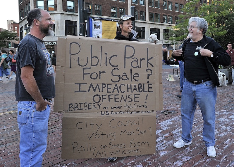 Sam Swenson, center, made this sign from some recycled cardboard and chats with two attendees at the event, which organizers hope will help mobilize support to keep Congress Square Plaza public.