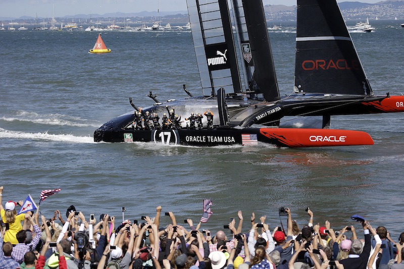 The crew on Oracle Team USA celebrates after winning the 19th race against Emirates Team New Zealand to win the America's Cup sailing event, as fans wave in the foreground Wednesday, Sept. 25, 2013, in San Francisco.