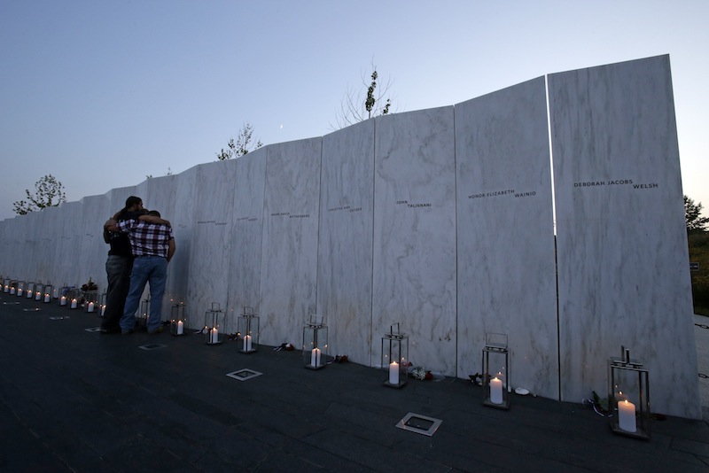 Visitors embrace in front of the wall containing the 40 names of the crew and passengers of Flight 93 at the Flight 93 National Memorial during a candlelight remembrance on Tuesday, September 10, 2013. (AP Photo/Gene J. Puskar)