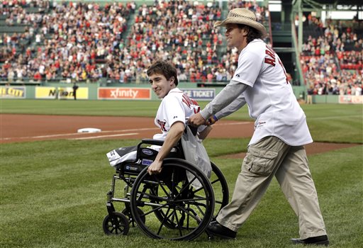 Boston Marathon bombing survivor Jeff Bauman is wheeled onto the field by Carlos Arredondo, the man who helped save his life, to throw out the ceremonial first pitch at Fenway Park on May 28, 2013.