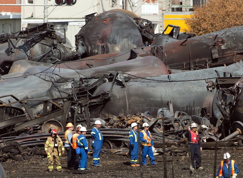 In this Tuesday, July 16, 2013 file photo, workers stand before mangled tanker cars at the crash site of a train derailment and fire in Lac-Megantic, Quebec, that happened on July 6. The bankrupt railroad whose runaway train sparked a fire and explosion that killed 47 people in Quebec could be sold by year's end, the company's trustee said Thursday.. (AP Photo/Ryan Remiorz, Pool, File)