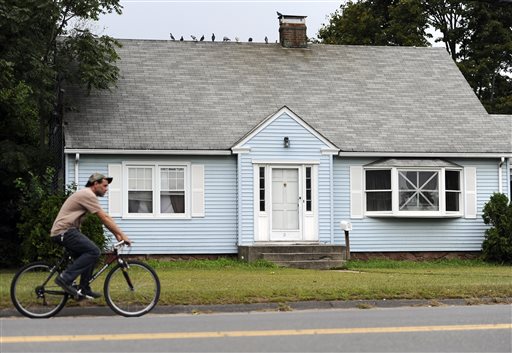 A man rides a bicycle by a house owned by the uncle of former New England Patriots' tight end Aaron Hernandez, in Bristol, Conn. A group of people who all have ties to the small cape-style home have become central figures in the investigations linking former New England Patriot Hernandez to two murder cases.