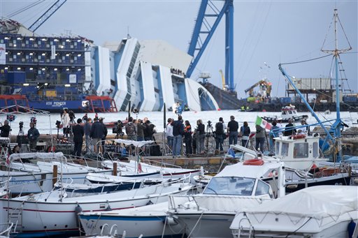 Reporters watch the Costa Concordia ship lying on its side on the Tuscan Island of Giglio, Italy, early Monday morning. An international team of engineers is trying a never-before attempted strategy to set upright the luxury liner, which capsized after striking a reef in 2012, killing 32 people.