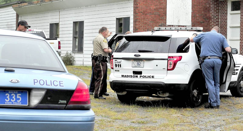 Somerset County deputy sheriffs, center, and a Maine State Police trooper, right, speak to James L. Mayo, inside a Madison Police Department cruiser, who was arrested near the Cornville Regional Charter School on Monday.