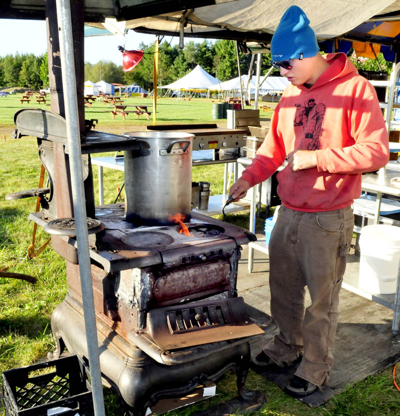Don Gardner stokes a woodstove with firewood while making yogurt at the Maine Falafel company food booth in preparation for the three-day Common Ground Country Fair in Unity that begins this Friday.
