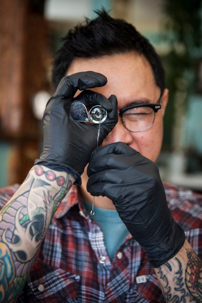 Using a magnifying “needle eye loupe,” a tool of the trade, Phuc Tran inspects a needle for flaws or damage that could cause infection.