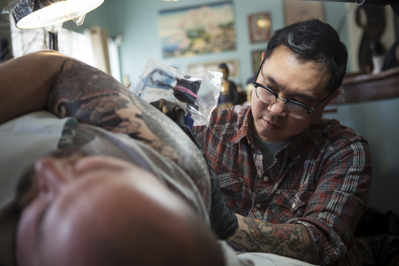 Phuc Tran works with a customer at his Tsunami Tattoo.