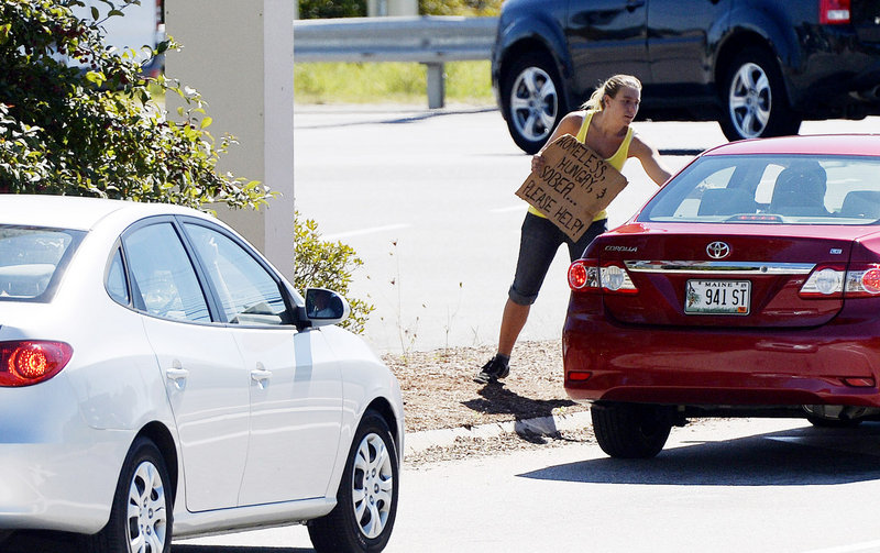 A woman accepts money from a motorist Friday while panhandling from a median on Route 111 in Biddeford. Her sign reads: “Homeless, hungry, & sober ... Please help!”