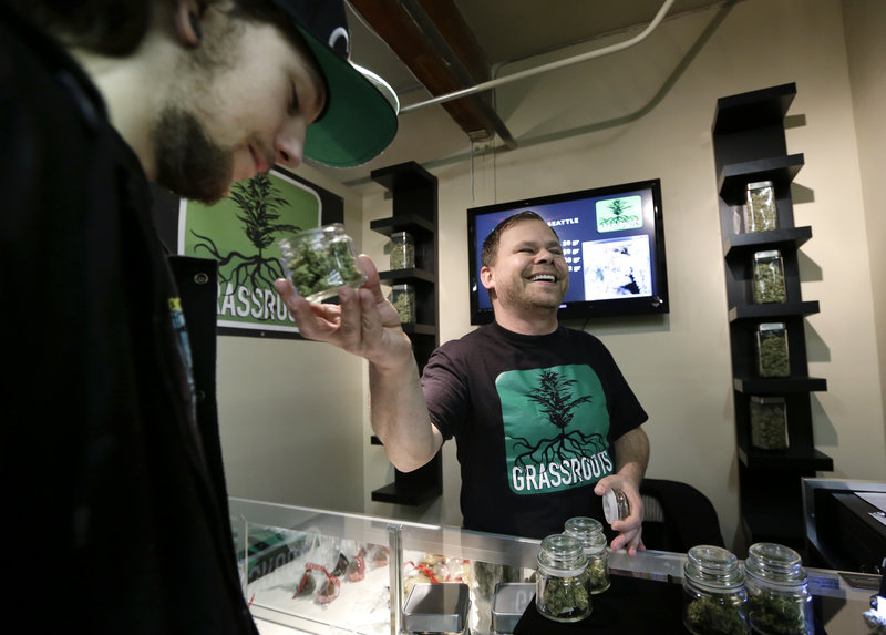 Vendor Jeff Simmons, right, smiles as he holds up a jar of marijuana for Dylan Tracy to sniff during the grand opening of the Seattle location of the Northwest Cannabis Market for sales of medical marijuana products on Feb. 13.