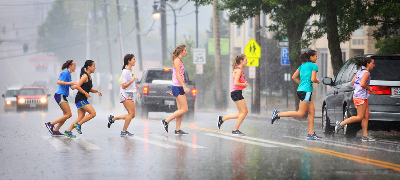 Members of the Portland High School girls’ cross-country team dash across Cumberland Avenue Thursday after a drenching training run.
