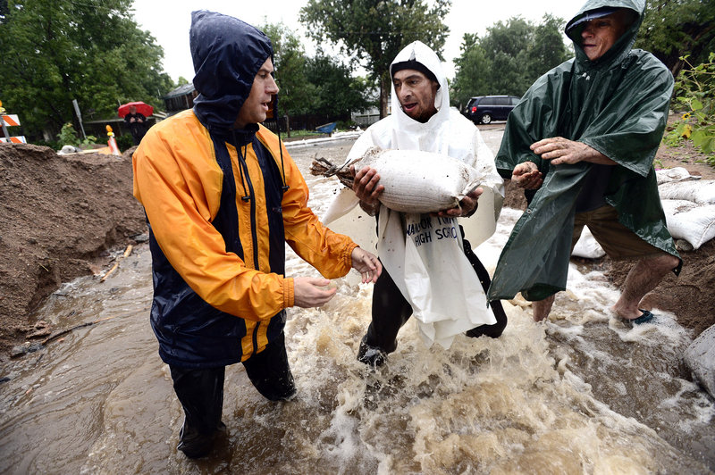 Dan Feldheim, from left, Scott Hoffenberg and John Smart pass sandbags Sunday as residents reinforce the dam on University Hill in Boulder, Colo. Surging waters have left four people dead and two missing and presumed dead.