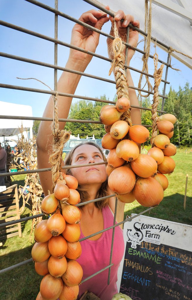 Emily Goodchild, from Stonecipher Farm in Bowdoinham, hangs strings of onions on their stall at the Common Ground Fair on Friday.