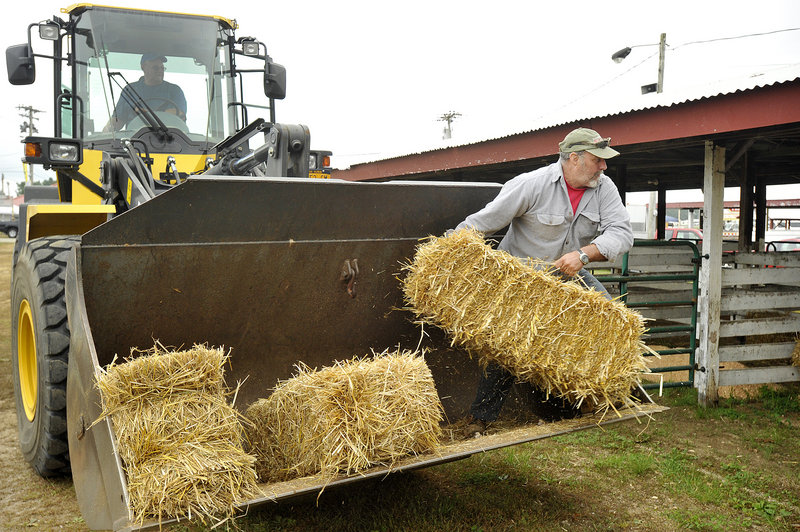 Fair worker Mike Haskell of Windham tosses bales of hay into stalls awaiting the animals’ arrival. Fellow fair worker Steve Googins of Gray is manning the front-end loader.