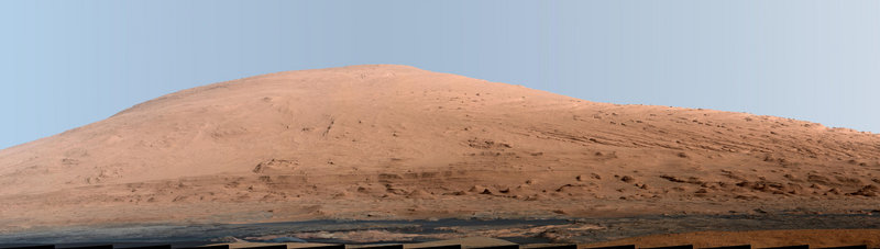 A portion of Mount Sharp rises from Mars’ stark landscape in this photo taken by Curiosity last year. NASA enhanced the image to give better definition to the terrain, but distorted the color of the sky by giving it a blue hue. It is one of many photos sent back by Curiosity that are helping scientists to learn more about the planet.