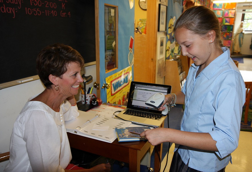 Jenny Hall, left, head librarian and volunteer at Holy Cross Catholic School in South Portland, helps student Emma Langevin check the barcode on a book as part of the school library’s recent upgrade to make more than 4,000 books available via Web-based software.