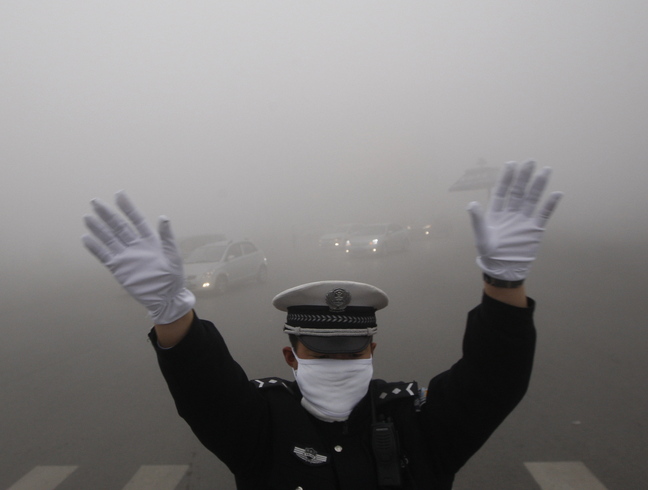 A traffic policeman signals to drivers during a smoggy day in Harbin, Heilongjiang province, on Monday. The second day of heavy smog has forced the closure of schools and highways.