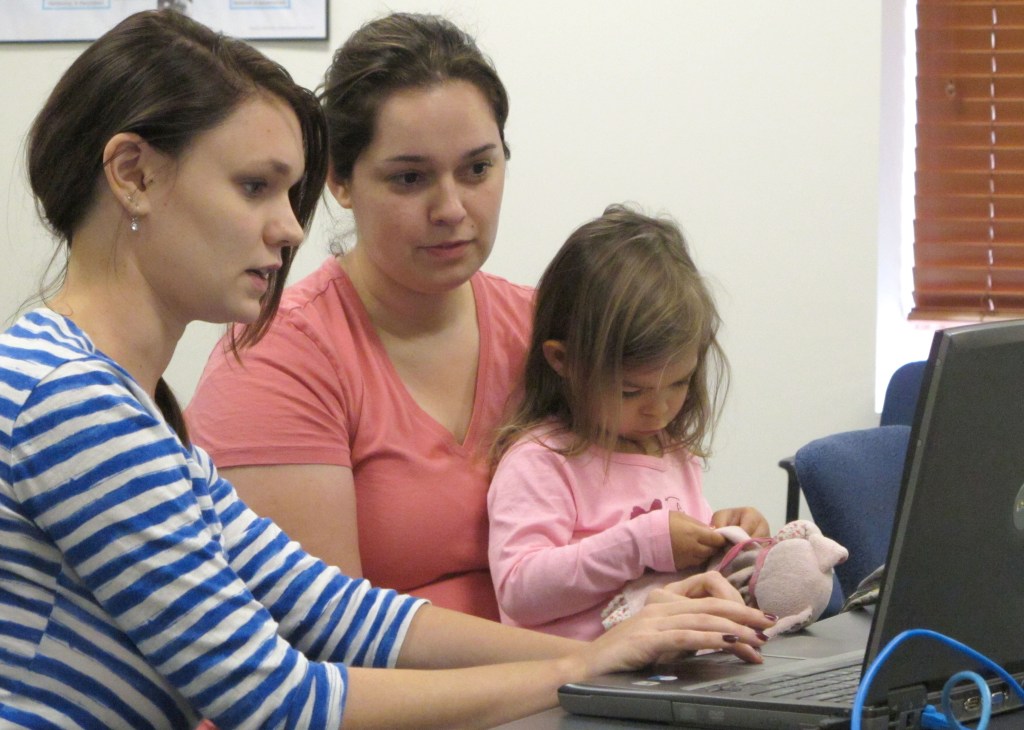 Debora Costa right, tries to sign up for insurance coverage for her two children, including 2-year-old Victoria, Wednesday, Oct. 2, 2013, with help from Champaign Urbana Public Health District employee Alice Cronenberg in Champaign, Ill. Costa, who recently moved to Illinois from Brazil with her graduate-student husband and children, found after about 10 minutes that she didn’t have all the information she would need to sign up.