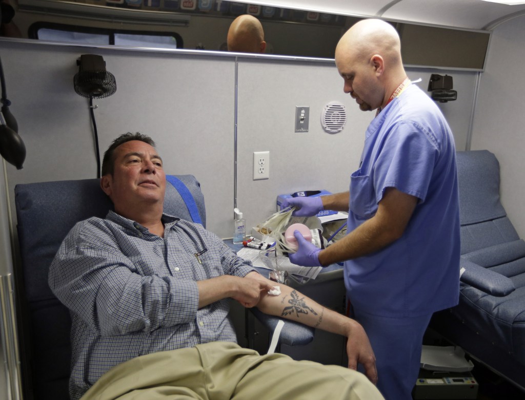 Technician Greg Snyder, right, finishes up a blood draw from Chris Page after he donated blood in an Indiana Blood Center Bloodmobile in Indianapolis recently. The Indiana Blood Center announced in June 2013 that it would reduce its mobile operations, close a donor center and cut other costs because demand from hospitals had fallen 24 percent from the previous year.