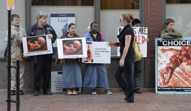 A pedestrian walks past anti-abortion protesters on Congress St. in Portland near the Planned Parenthood clinic Friday, Oct. 04, 2013.