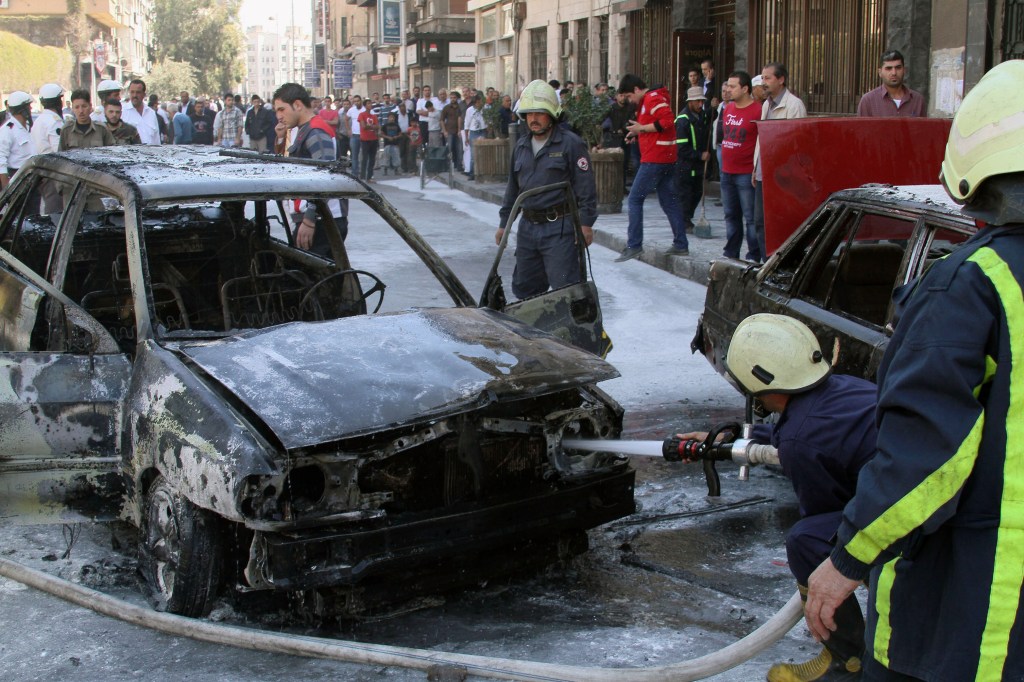 Firefighters extinguish a burning vehicle after two mortar rounds struck the Abu Roumaneh area in Damascus, Syria, Saturday, Oct. 12, 2013. Syriaís state news agency said two mortar rounds struck an upscale neighborhood in the Syrian capital of Damascus, killing at least one child and injuring a dozen people.