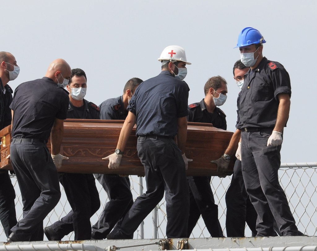 The casket of migrant who died when a packed fishing boat capsized in the Canal of Sicily is carried aboard a Italian Navy ship at the Lampedusa island harbor Saturday.