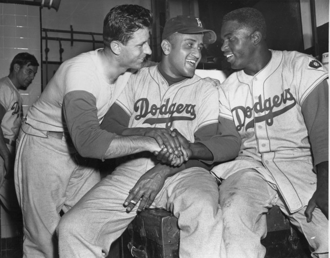 Brooklyn Dodgers baseball player Andy Pafko, left, Don Newcomb, center, and Jackie Robinson shake hands in their dressing room after the Dodgers beat the Philadelphia Phillies 5-0, in New York. That flowing blue “Dodgers” script across the front of the jersey that followed them from Brooklyn.