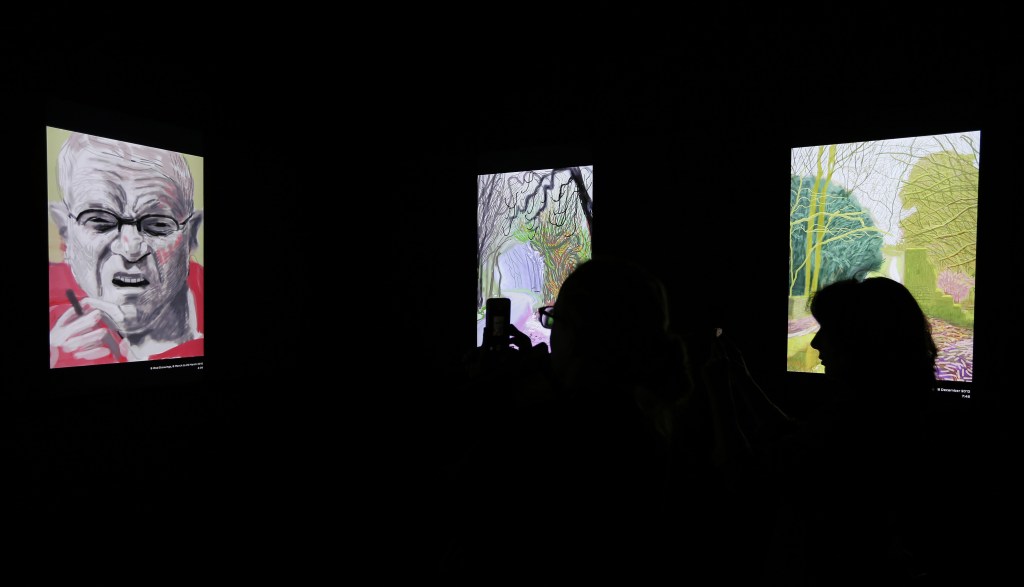 In this photo taken Thursday, Oct. 24, 2013, people watch how a painting made by David Hockney using an iPad takes shape at an exhibit in San Francisco. A sweeping new exhibit of Hockneyís work, including about 150 iPad images, has opened in the deYoung Museum in Golden Gate Park, just a short trip for Silicon Valley techies who created both the hardware and software for this magnificent reinvention of fingerpainting.