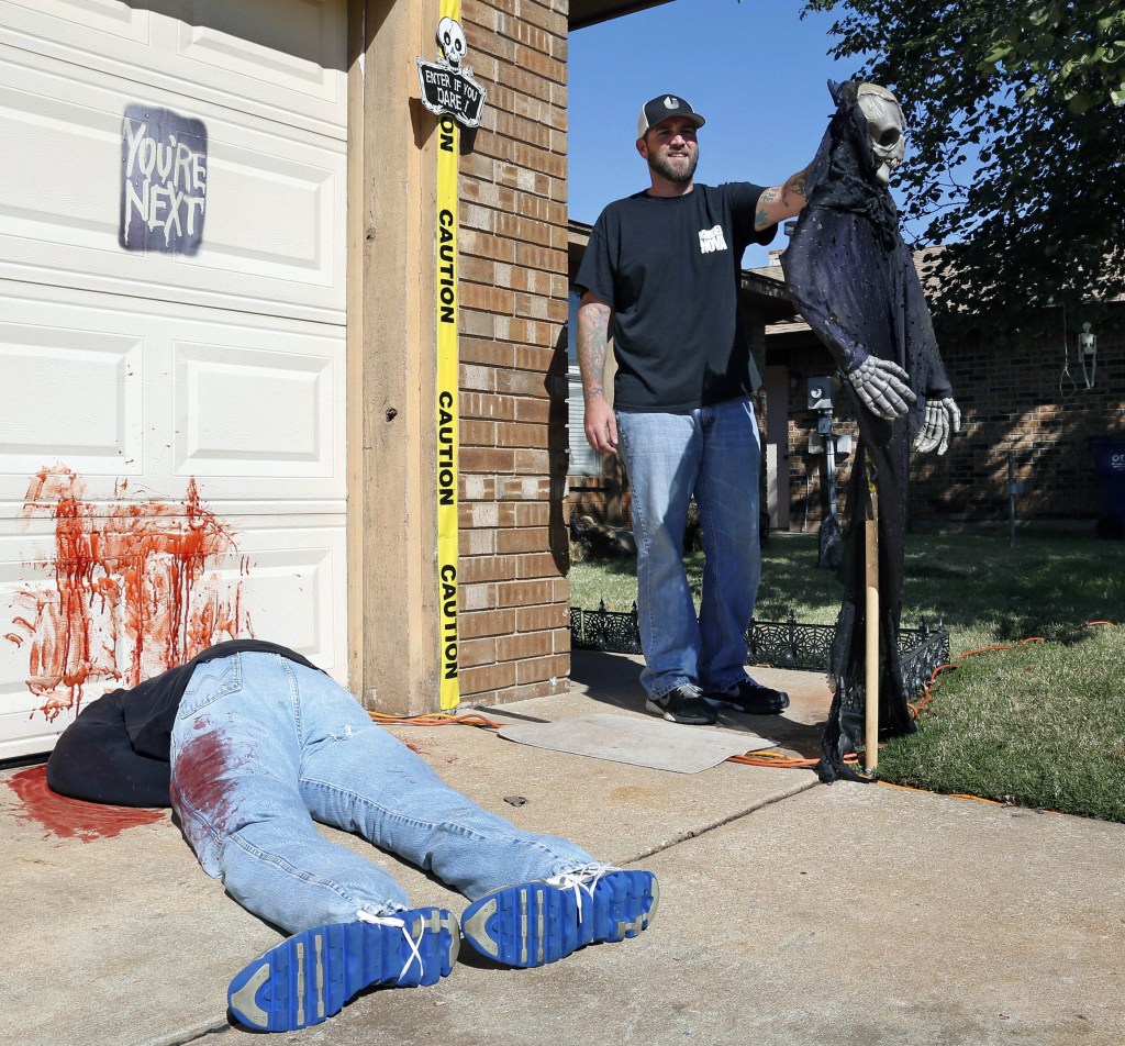 Johnnie Mullins stands Thursday with his controversial Halloween display featuring headless dummies dressed in his work clothes at his home in Mustang, Okla.