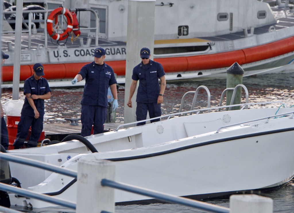Coast Guard personnel inspect a vessel with a missing center console that capsized early Wednesday about seven miles east of Miami, killing four of the 15 people on board.