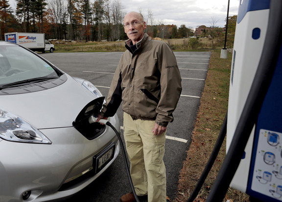 Marc Lausier, above, of Scarborough charges his Nissan Leaf, a fully electric car, at TideSmart Global in Falmouth on Friday. Gov. Paul LePage turned down Lausier’s offer to test drive the car. The photo at top shows the front end of the electric charger.