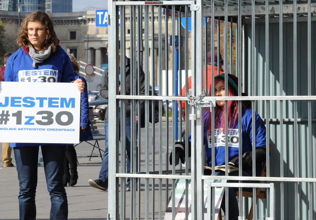 One Greenpeace activist sits in a cage in Warsaw, Poland, while another one holds a placard reading “I am 1 of the 30” in a protest against Russia’s jailing of Greenpeace activists.