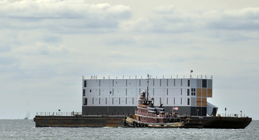A tugboat leads a barge carrying a mystery structure down the Thames River after it left New London, Conn., on Wednesday bound for Portland.