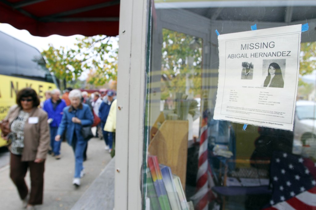 In this photo taken Wednesday Oct. 16, 2013, tourists walk by an information booth with a poster of missing teenager Abigail Hernandez in North Conway, N.H. Hernandez disappeared Wednesday Oct. 9 when she was last seen leaving school and walking towards home.)