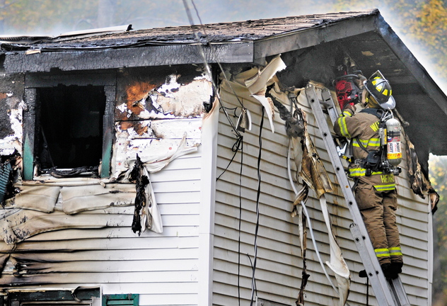 A firefighter cuts a hole to ventilate the attic of a home at 119 Granite Hill Road in Manchester on Saturday. The body of Sam Spinicci, 56, was found in a bedroom.