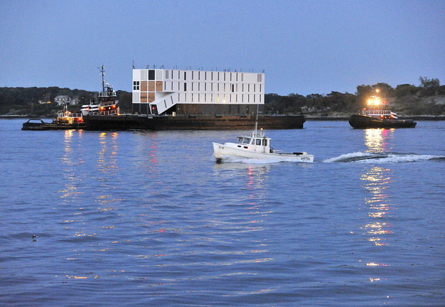 Tugboats tow a barge carrying a mystery structure into Portland Harbor at dusk Thursday. The structure was assembled on the barge in New London, Conn., and was headed for a Cianbro Corp. facility off Commercial Street in Portland, where it is scheduled for a significant amount of interior work before it is delivered to its owner.
