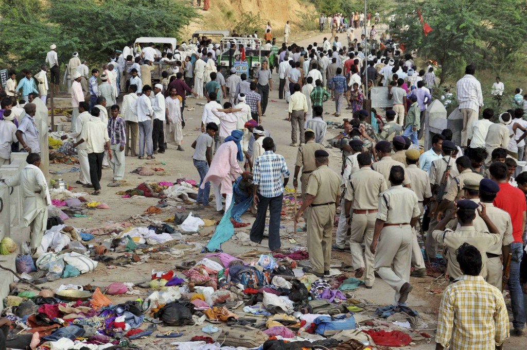 In this Sunday, Oct. 13, 2013 photo, Indian villagers gather as policemen, in uniform, arrive at the scene of a deadly stampede on a bridge across the Sindh River in Datia district in Madhya Pradesh state, India. Pilgrims visiting a temple for a popular Hindu festival in India stampeded on fears a bridge would collapse, and more than 100 people were crushed to death or died in the river below, officials said Monday. Scores more were injured, and some bodies may have washed away. (AP Photo)