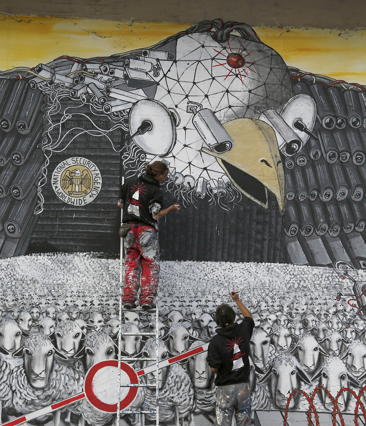 Artists A.Signl, left, and B. Shanti of the artist group Captain Borderline paint their mural 'Surveillance of the fittest' at a wall in Cologne, Germany, Thursday. The painting, showing an American bald eagle with surveillance cameras watching a herd of sheep, is aimed at drawing attention to the spying program of the American National Security Agency.