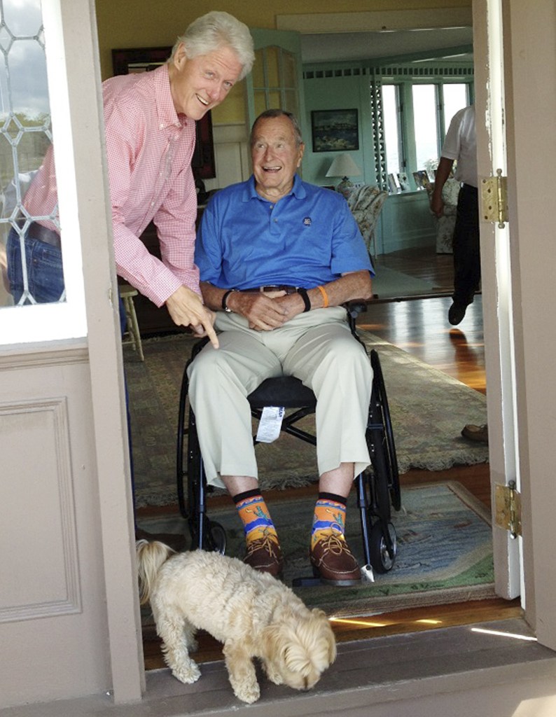 Former President Bill Clinton points to western-themed socks worn by former President George H.W. Bush at Bush’s home in Kennebunkport during a visit last month. Bush has donated the socks, an autographed picture of the moment and a signed letter of authenticity to a charity auction for the Roman Catholic Diocese of Portland.