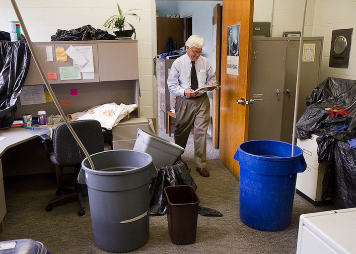 Rob Wood, director of Portland’s Adult Education Program, reviews a document in his office near barrels set up to collect water in June from a leaking roof at the West School. Gov. Paul LePage’s government efficiency agency is recommending a $9.5 million cut for public school districts in order to balance the state’s budget.