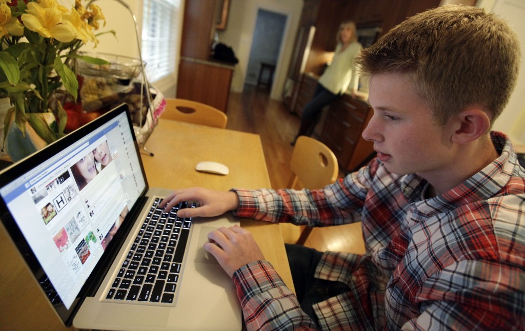 Mark Risinger, 16, checks his Facebook page on his computer as his mother, Amy Risinger, looks on at their home in Glenview, Ill. An influential pediatricians' group says unrestricted media use has been linked with violence, cyberbullying, school woes, obesity, lack of sleep and a host of other problems.