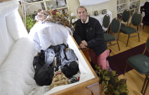 Anne Cote sits in the haunted funeral parlor she’s created at her home in Falmouth. Cote likes Halloween because it lets people explore scary themes while “controlling the horror.”